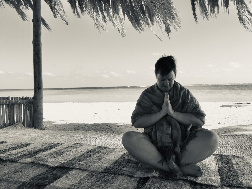 Zoe sitting on a mat with her head bowed and her hands in prayer