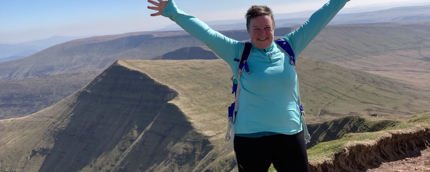 Zoe on a mountain top with her arms outstretched