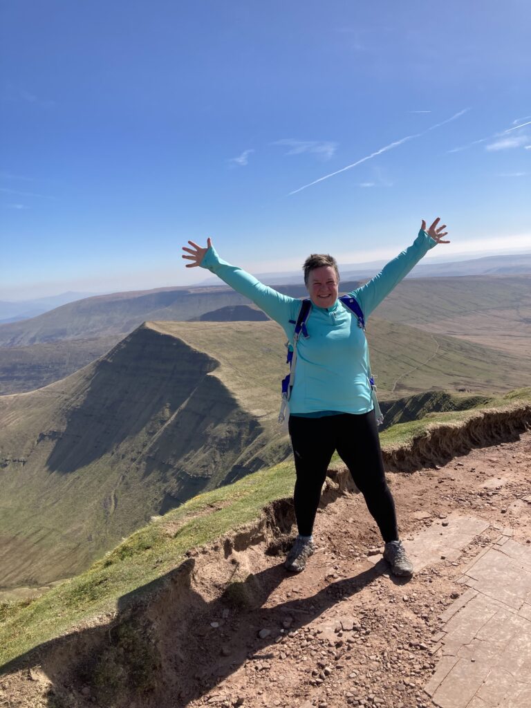 Zoe on a mountain top with her arms outstretched